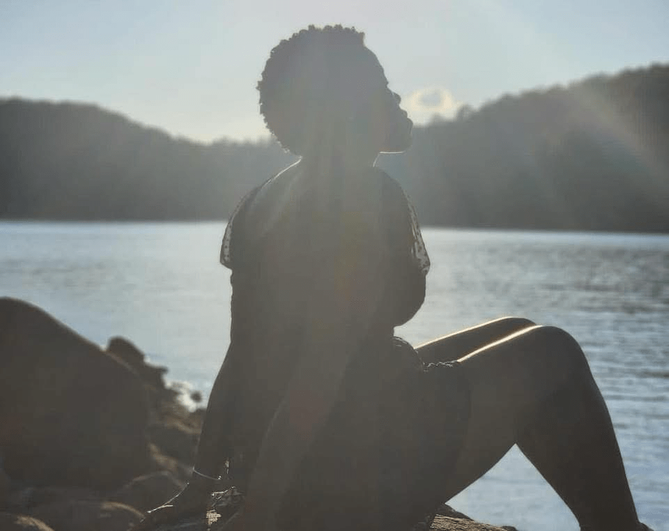 Silhouette of a picture me sitting peacefully by a lake at sunset, bathed in soft natural light - symbolizing reflection, spiritual sensitivity and healing. 